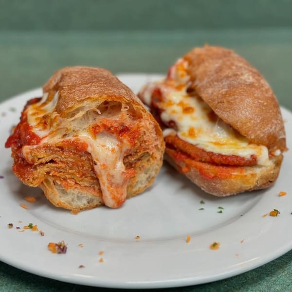Two Cousins Pizza chicken parmesan subs, overflowing with melted cheese and red sauce, on a white plate.