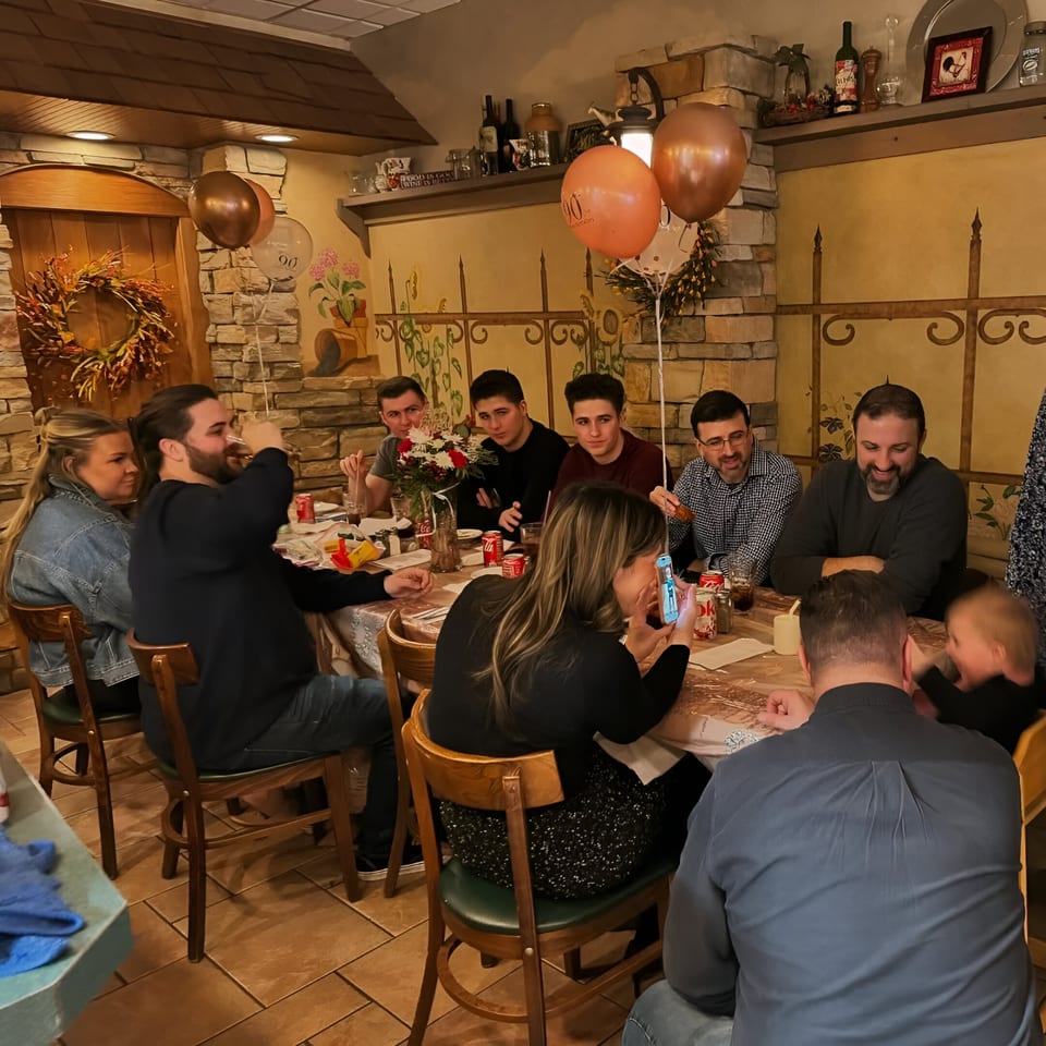 A group of people celebrating a birthday at a long table inside Cousins Pizza restaurant.