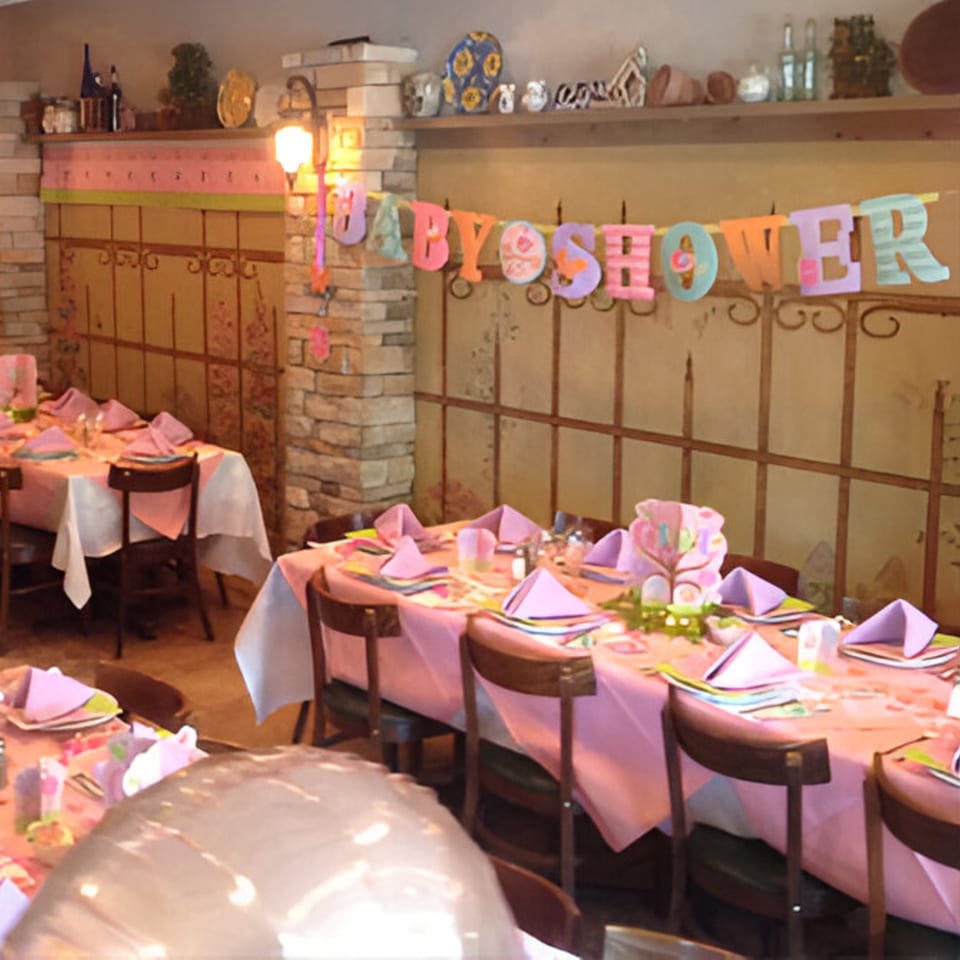 Restaurant dining room set up for a baby shower with pink tablecloths and a "BABY SHOWER" banner.