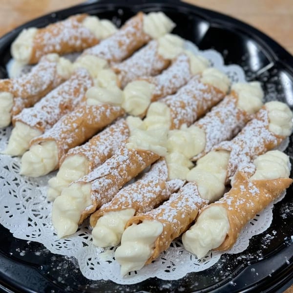 A platter of Cousins Pizza cannolis, filled with cream and dusted with powdered sugar.
