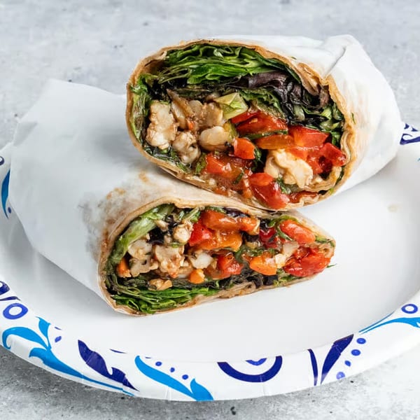 Two halves of a chicken and vegetable wrap on a white paper plate with blue designs.