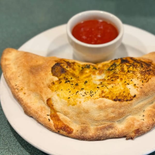 Golden-brown calzone with herbs on a white plate, served with a side of red marinara sauce.