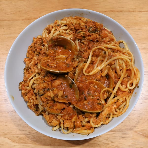A white bowl filled with linguine pasta, red sauce, and clams on a wooden table.