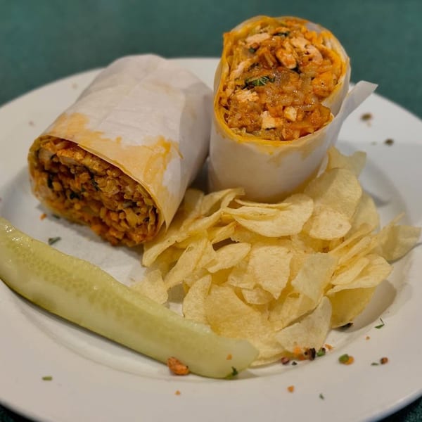 Two Cousins Pizza wraps, one open, with chips and a pickle spear on a white plate.